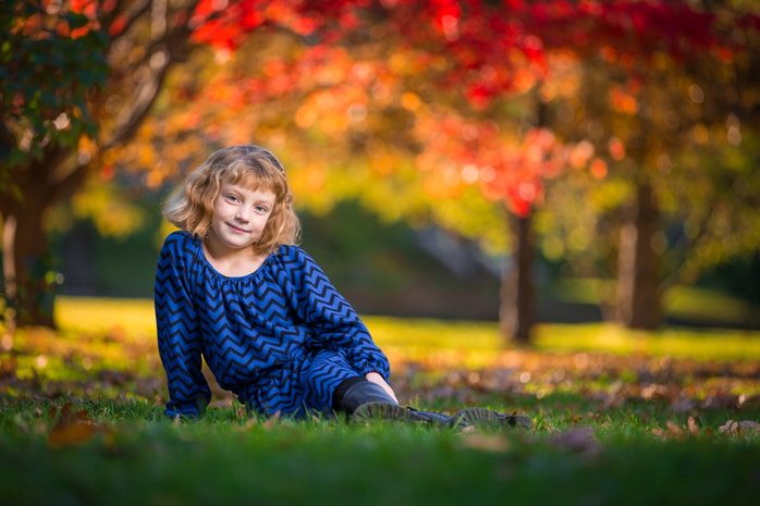 A young girl smiling brightly as she is lifted into the air amidst fallen autumn leaves.