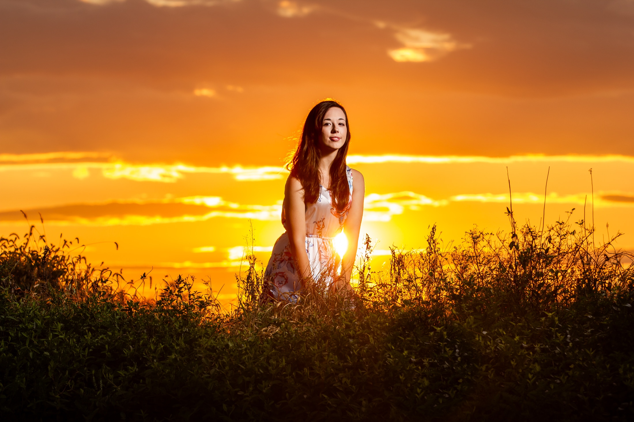 Senior girl looks at camera and smiles in golden sun
